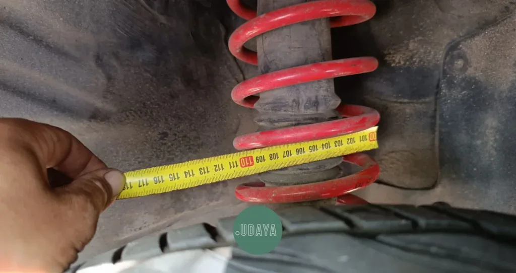 Amortiguador con resorte rojo y cinta métrica midiendo la distancia en la suspensión del vehículo.