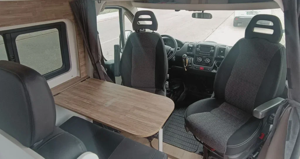 Vehículo camper convertido con zona de comedor y asientos cómodos, ideal para viajes y descanso.