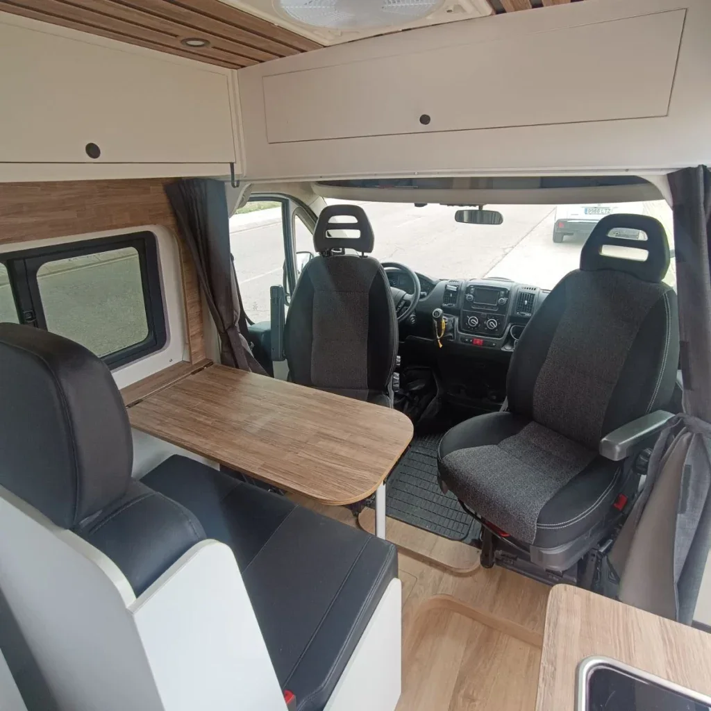 Interior de una campervan con zona de cocina y asientos convertibles para descanso y comidas, diseñada para viajes cómodos y funcionales.
