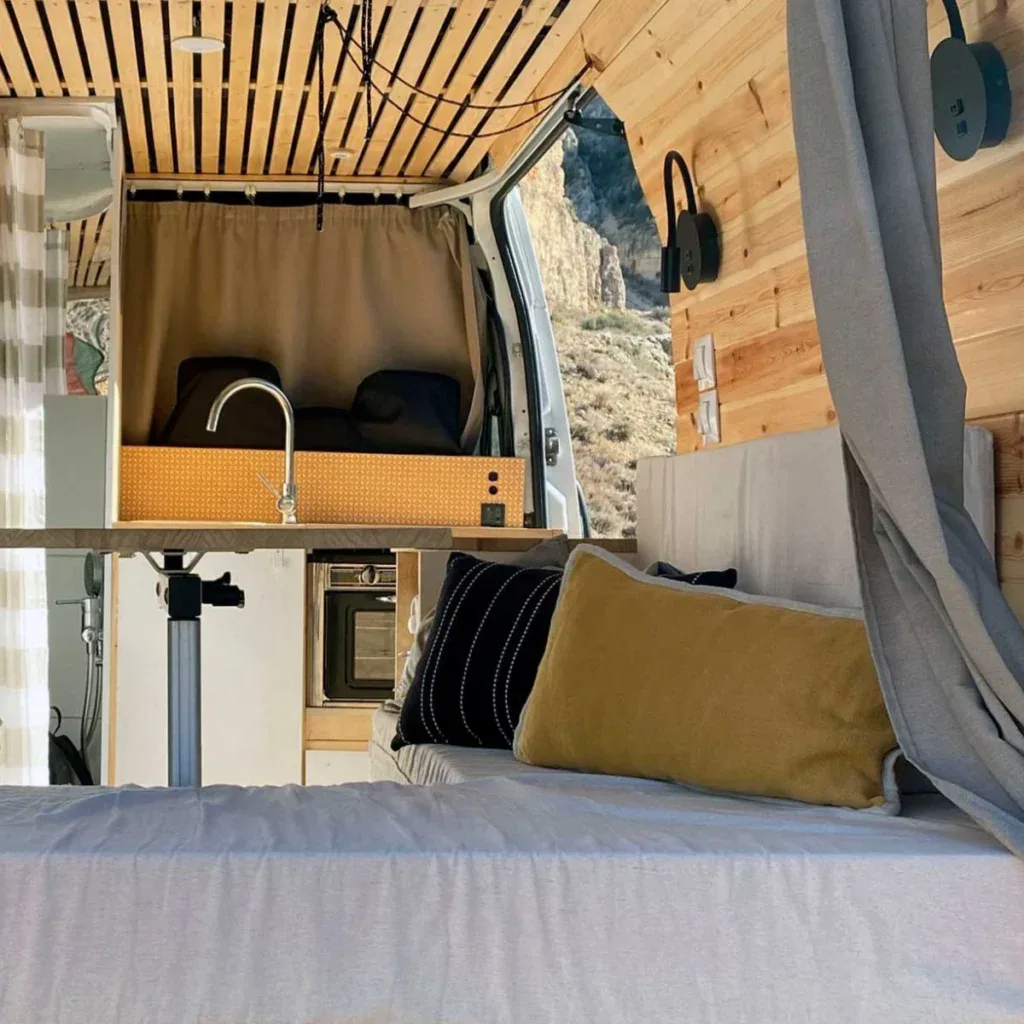Interior de furgoneta camper equipada con cocina, zona de descanso y ventanas panorámicas, ideal para viajes y vida nómada en vehículos homologados.