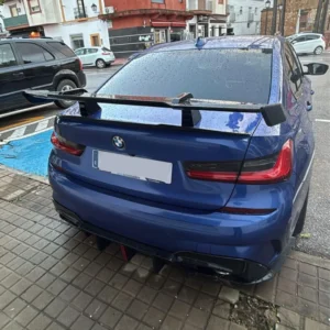 BMW Serie 3 azul con alerón trasero y lluvia en la superficie del coche, en un entorno urbano.