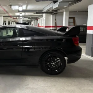 Coche deportivo negro en garaje con iluminación artificial y estructura de soporte, ideal para servicios de homologación de vehículos y conversiones de furgonetas camper.