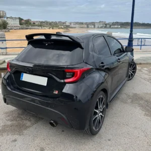 Coche compacto negro con modificaciones para homologación de vehículos y conversiones a camper van, en zona costera.